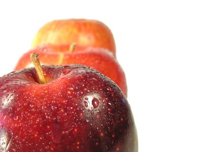 Nahaufnahme eines roten Apfels mit zwei dahinter stehenden Äpfeln auf weißem Hintergrund. Geringe Schärfentiefe.